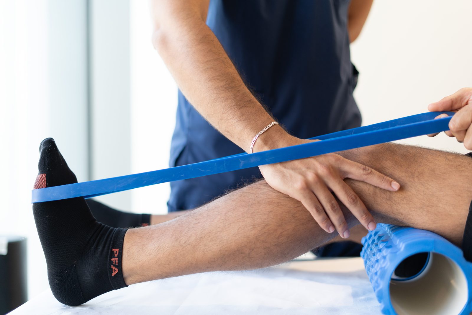 أخصائي علاج فيزيائي يوجّه تمرينًا بشريط المقاومة للساق ضمن التأهيل الرياضي في KINETIKA دبي هيلز